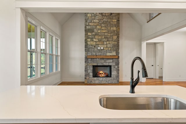 kitchen featuring lofted ceiling, light stone counters, hardwood / wood-style floors, sink, and a fireplace