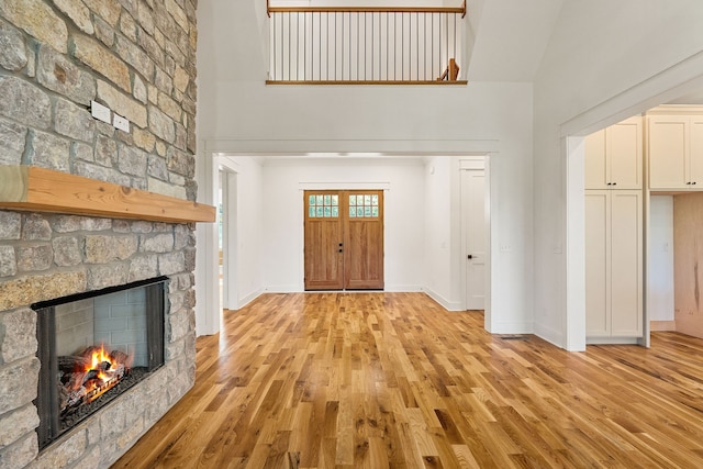 entrance foyer featuring light hardwood / wood-style floors, high vaulted ceiling, and a stone fireplace