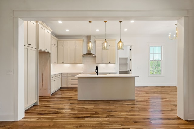 kitchen with wall chimney exhaust hood, dark wood-type flooring, a center island with sink, sink, and hanging light fixtures