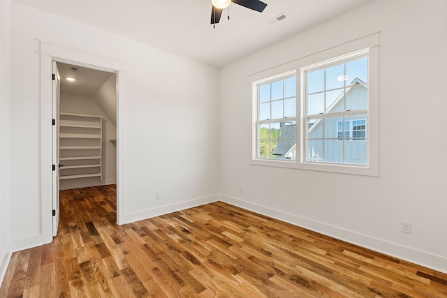 unfurnished bedroom with a spacious closet, ceiling fan, a closet, hardwood / wood-style flooring, and vaulted ceiling