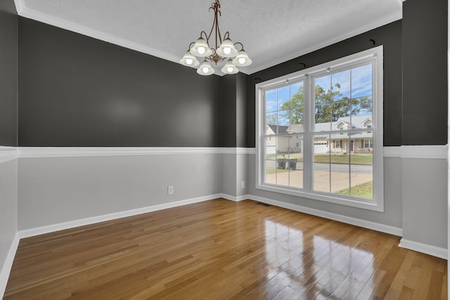 unfurnished dining area with hardwood / wood-style floors, an inviting chandelier, ornamental molding, and a textured ceiling