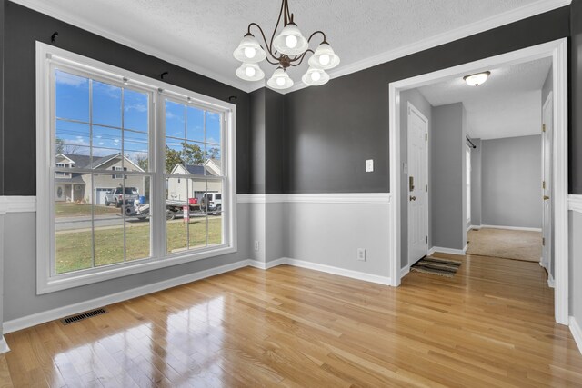 unfurnished dining area with a textured ceiling, a notable chandelier, ornamental molding, and light hardwood / wood-style flooring