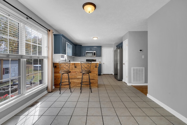 kitchen featuring stainless steel appliances, a healthy amount of sunlight, a breakfast bar, blue cabinets, and kitchen peninsula