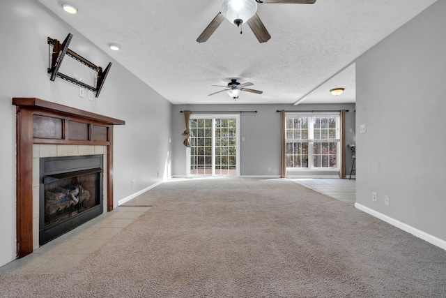 unfurnished living room featuring ceiling fan, light colored carpet, a textured ceiling, and a tiled fireplace