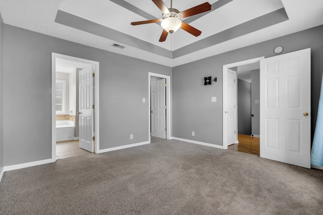 unfurnished bedroom with ceiling fan, light colored carpet, connected bathroom, and a raised ceiling