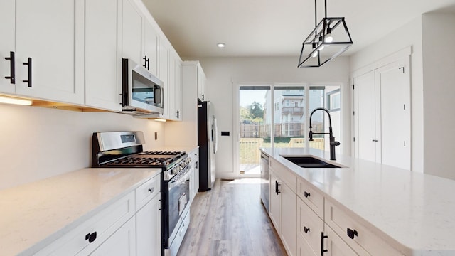 kitchen featuring light wood-type flooring, a sink, white cabinetry, stainless steel appliances, and hanging light fixtures