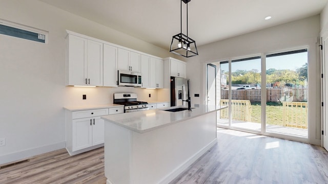 kitchen with an island with sink, decorative light fixtures, appliances with stainless steel finishes, and white cabinetry