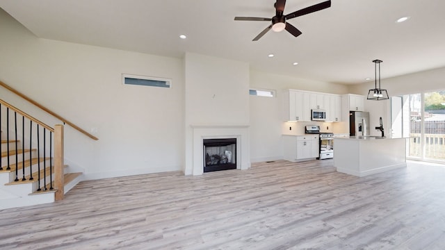 unfurnished living room with stairway, recessed lighting, a fireplace, and light wood-style floors