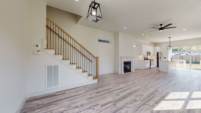 unfurnished living room with visible vents, baseboards, light wood-style flooring, and stairs