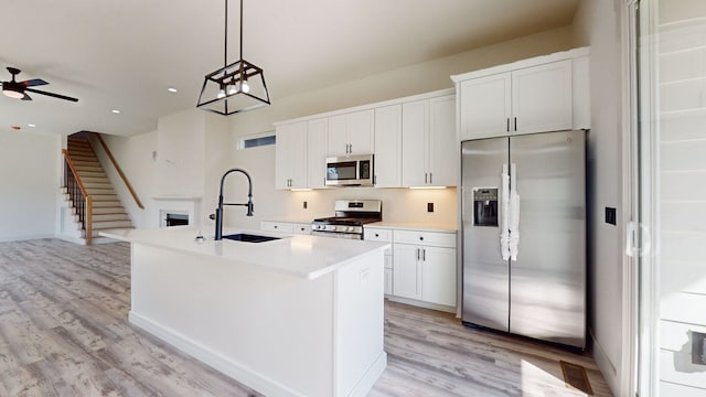 kitchen with a center island with sink, light wood-style flooring, appliances with stainless steel finishes, white cabinetry, and a sink