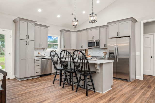 kitchen featuring lofted ceiling, a kitchen island, appliances with stainless steel finishes, a kitchen breakfast bar, and light hardwood / wood-style floors