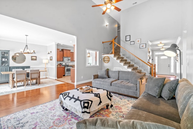 living room featuring a towering ceiling, ceiling fan with notable chandelier, and light hardwood / wood-style flooring