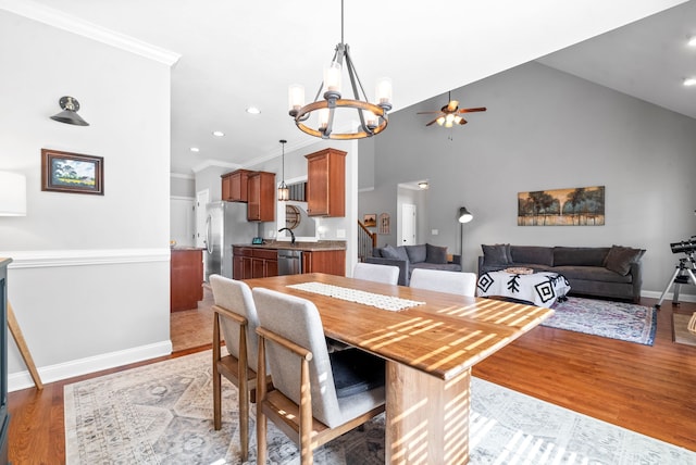 dining area featuring light wood-type flooring, ceiling fan with notable chandelier, sink, ornamental molding, and high vaulted ceiling