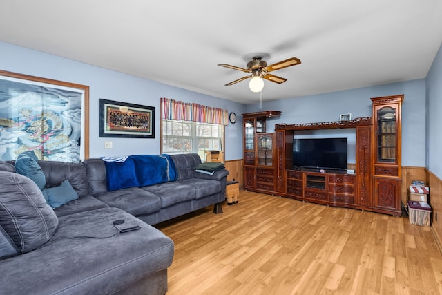 living room with wooden walls, ceiling fan, and light hardwood / wood-style floors