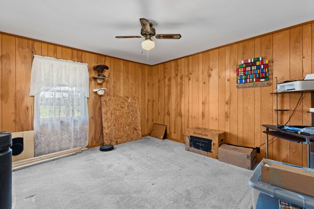 interior space featuring light colored carpet, ceiling fan, and wood walls