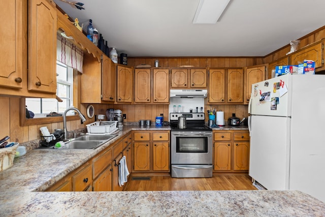 kitchen featuring stainless steel electric range oven, sink, white fridge, wooden walls, and light wood-type flooring