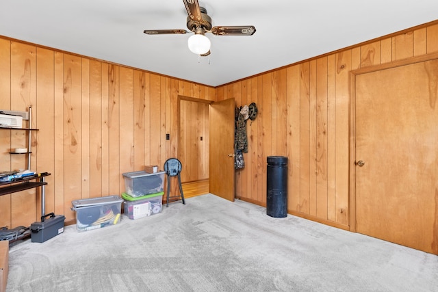 misc room featuring wooden walls, ceiling fan, and light carpet