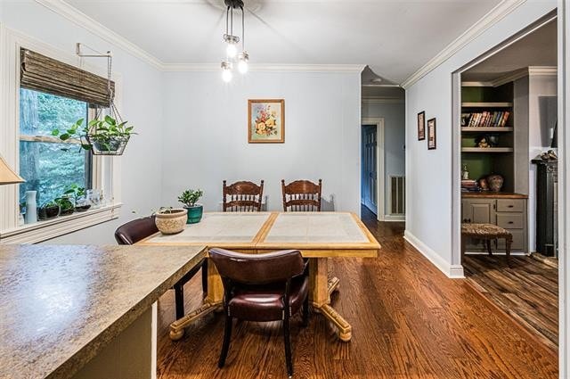 dining area featuring dark wood-type flooring, crown molding, and built in shelves