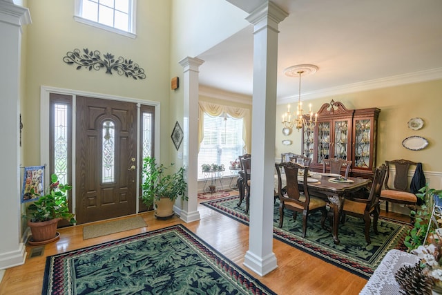 entryway featuring decorative columns, wood-type flooring, ornamental molding, and a notable chandelier