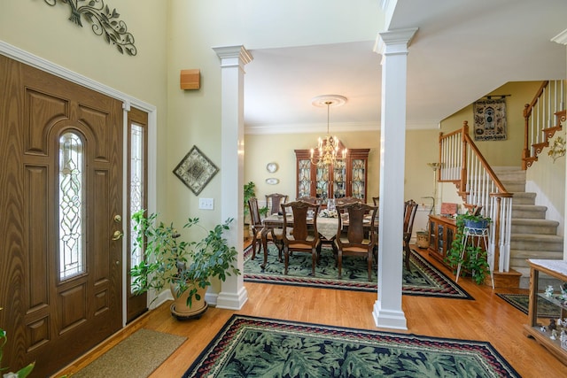 entrance foyer featuring crown molding, hardwood / wood-style flooring, an inviting chandelier, and ornate columns