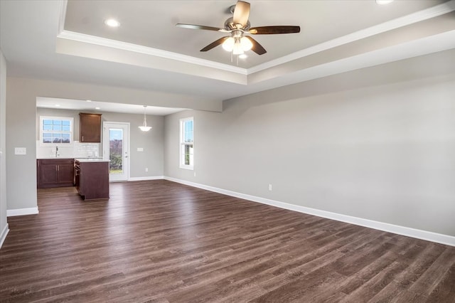 unfurnished living room featuring dark hardwood / wood-style floors, crown molding, ceiling fan, and a tray ceiling