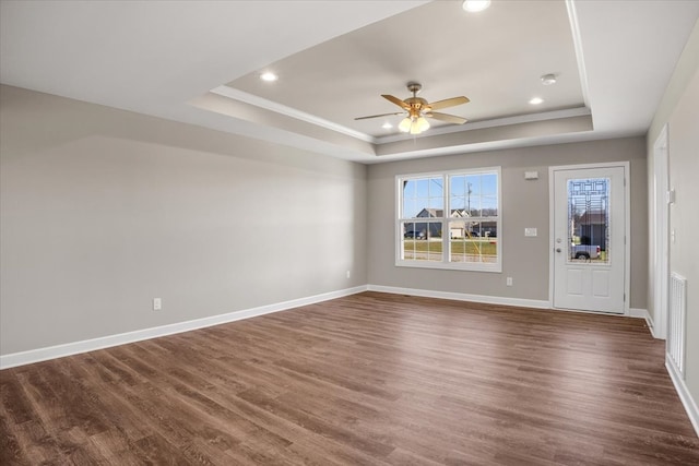 unfurnished living room with a tray ceiling, ceiling fan, and dark wood-type flooring