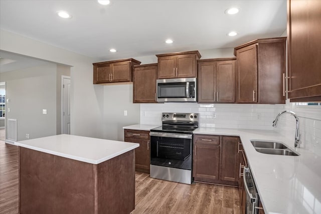 kitchen with sink, a center island, hardwood / wood-style floors, decorative backsplash, and appliances with stainless steel finishes