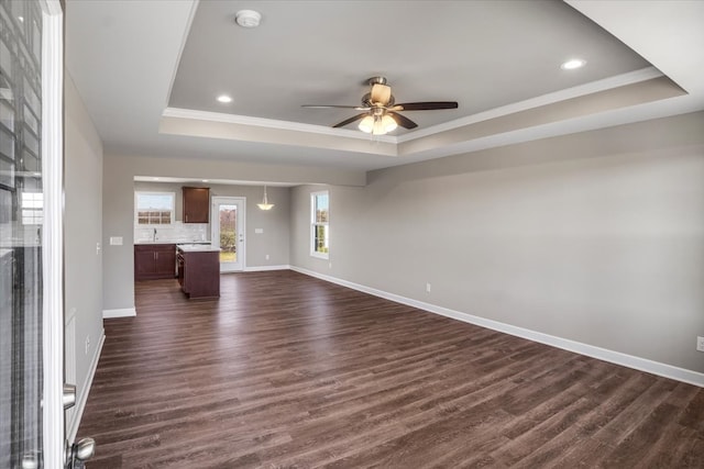 unfurnished living room featuring ceiling fan, a raised ceiling, ornamental molding, and dark wood-type flooring