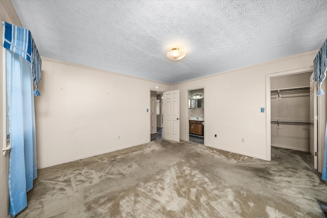 unfurnished bedroom with carpet floors, a textured ceiling, connected bathroom, a closet, and a walk in closet