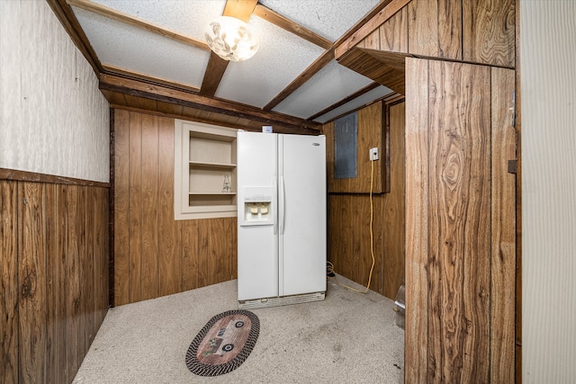 interior space with a textured ceiling, white fridge with ice dispenser, electric panel, light colored carpet, and wooden walls