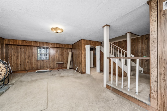 basement featuring wooden walls, a textured ceiling, and light colored carpet