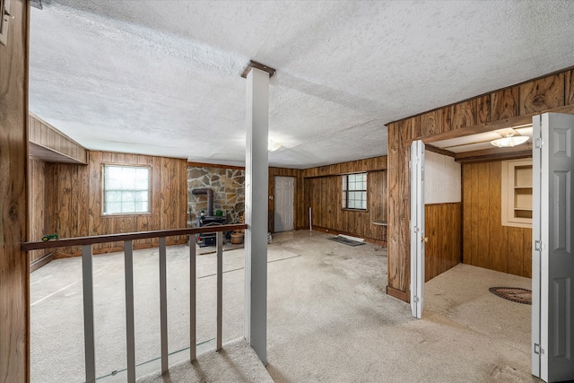 basement featuring a wood stove, carpet flooring, wood walls, and a textured ceiling