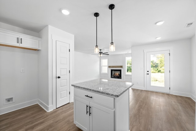 kitchen with light wood-type flooring, ceiling fan, a multi sided fireplace, light stone countertops, and white cabinetry