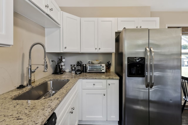 kitchen with light stone counters, stainless steel fridge with ice dispenser, white cabinetry, and sink