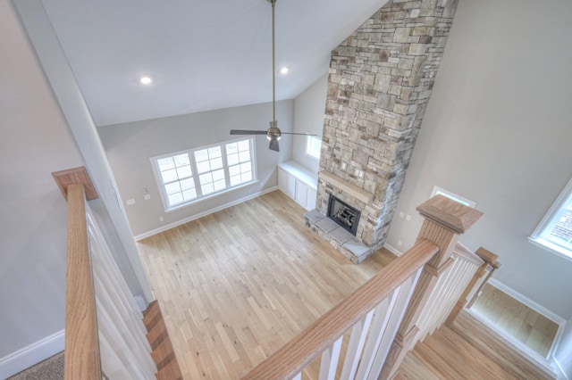 living room with ceiling fan, a stone fireplace, vaulted ceiling, and light hardwood / wood-style flooring