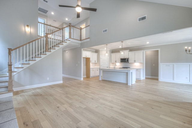 unfurnished living room with ceiling fan with notable chandelier, high vaulted ceiling, sink, and light hardwood / wood-style floors