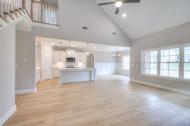 unfurnished living room featuring ceiling fan with notable chandelier, sink, high vaulted ceiling, and light hardwood / wood-style flooring