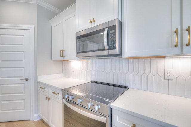 kitchen with white cabinetry, light stone counters, light hardwood / wood-style flooring, ornamental molding, and stainless steel appliances