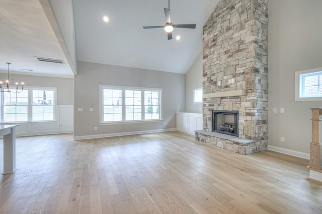 unfurnished living room featuring ceiling fan with notable chandelier, a fireplace, high vaulted ceiling, and light wood-type flooring