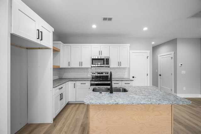 kitchen with appliances with stainless steel finishes, light hardwood / wood-style flooring, white cabinets, and a kitchen island with sink