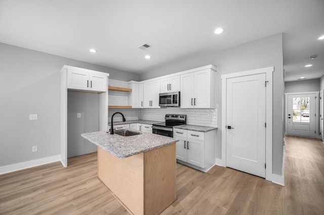 kitchen featuring stainless steel appliances, a center island with sink, sink, light wood-type flooring, and white cabinets