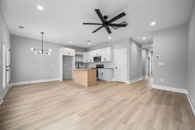 kitchen with white cabinets, hanging light fixtures, appliances with stainless steel finishes, a kitchen island with sink, and light wood-type flooring