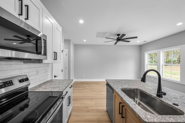 kitchen with light stone countertops, sink, stainless steel appliances, white cabinets, and light hardwood / wood-style flooring