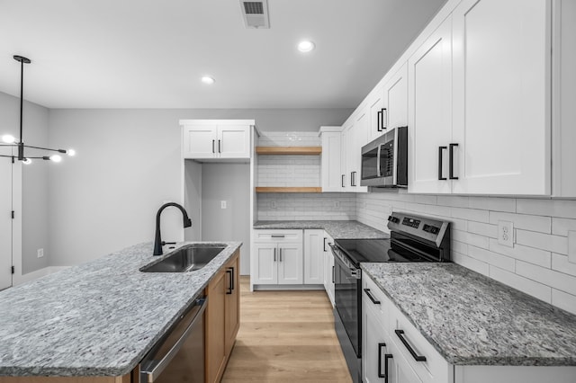 kitchen featuring white cabinets, an island with sink, appliances with stainless steel finishes, sink, and decorative light fixtures