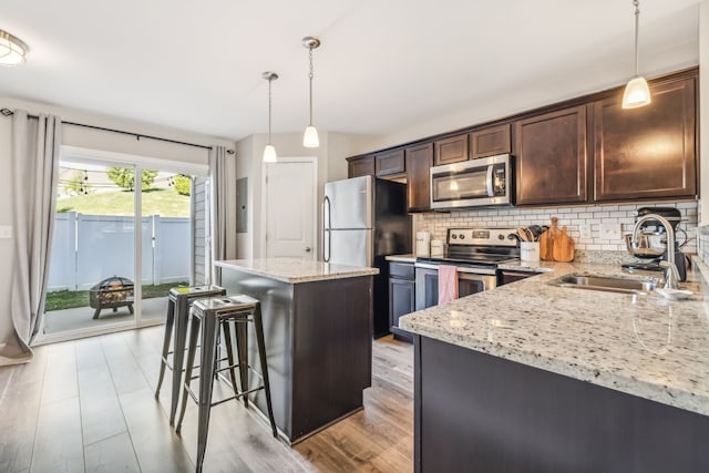 kitchen with dark brown cabinetry, sink, a kitchen island, decorative light fixtures, and appliances with stainless steel finishes