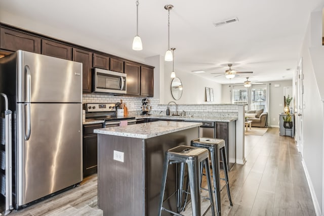 kitchen with a center island, stainless steel appliances, a breakfast bar area, light hardwood / wood-style flooring, and dark brown cabinets