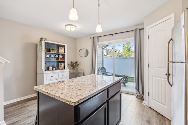 kitchen with light stone counters, pendant lighting, a kitchen island, stainless steel refrigerator, and light wood-type flooring