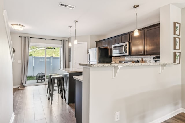 kitchen with light wood-type flooring, light stone countertops, stainless steel appliances, pendant lighting, and a breakfast bar area