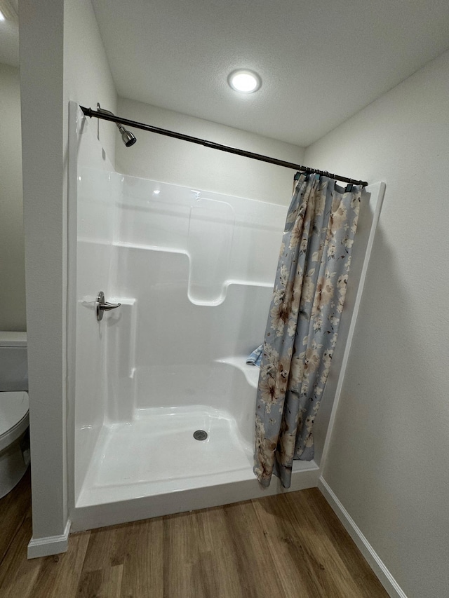 bathroom featuring hardwood / wood-style flooring, toilet, curtained shower, and a textured ceiling