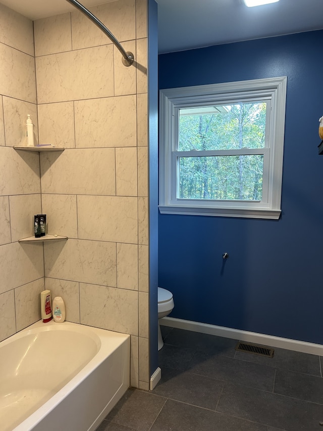 bathroom featuring tile patterned flooring, toilet, and tiled shower / bath combo